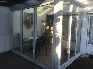 Ein durch Glaswände geschützter Patio-Bereich mit Tisch und Stühlen, einer Lampe und einer dekorativen Wandgestaltung.