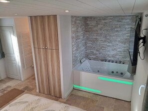 A modern bathroom with a wooden wardrobe, a stone-textured wall, and a bathtub with green lighting.