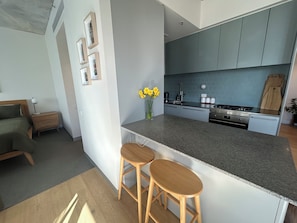 A modern kitchen with a central island, bar stools, and a dining area with a bed. - Sunlit 2BD Apartment with Parking, Brunswick (Brunswick)
