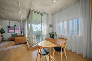 Un espace de vie moderne comprenant un coin repas, un canapé, une table basse et une grande fenêtre avec des rideaux.