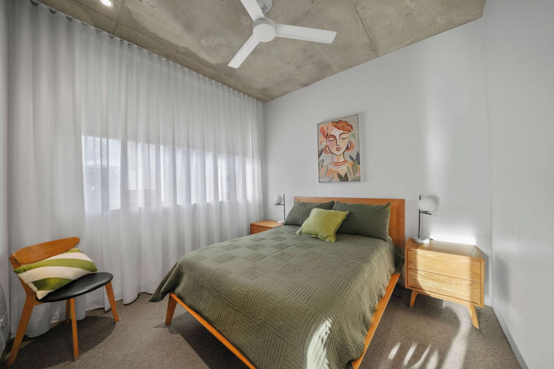 A bedroom with a bed, a chair, a bedside table, a floor lamp, and a ceiling fan.