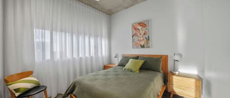 A bedroom with a bed, a chair, a bedside table, a floor lamp, and a ceiling fan.