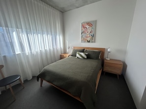 A bedroom with a bed, two bedside tables, a chair, a window with curtains, and a wall art piece. - Sunlit 2BD Apartment with Parking, Brunswick (Brunswick)