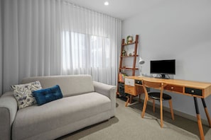 A modern living room with a sofa, a wooden desk, a computer, and a bookshelf. - Sunlit 2BD Apartment with Parking, Brunswick (Brunswick)
