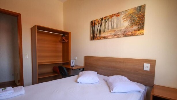 Habitación de hotel con cama, un cuadro de un bosque, un armario de madera y un escritorio.