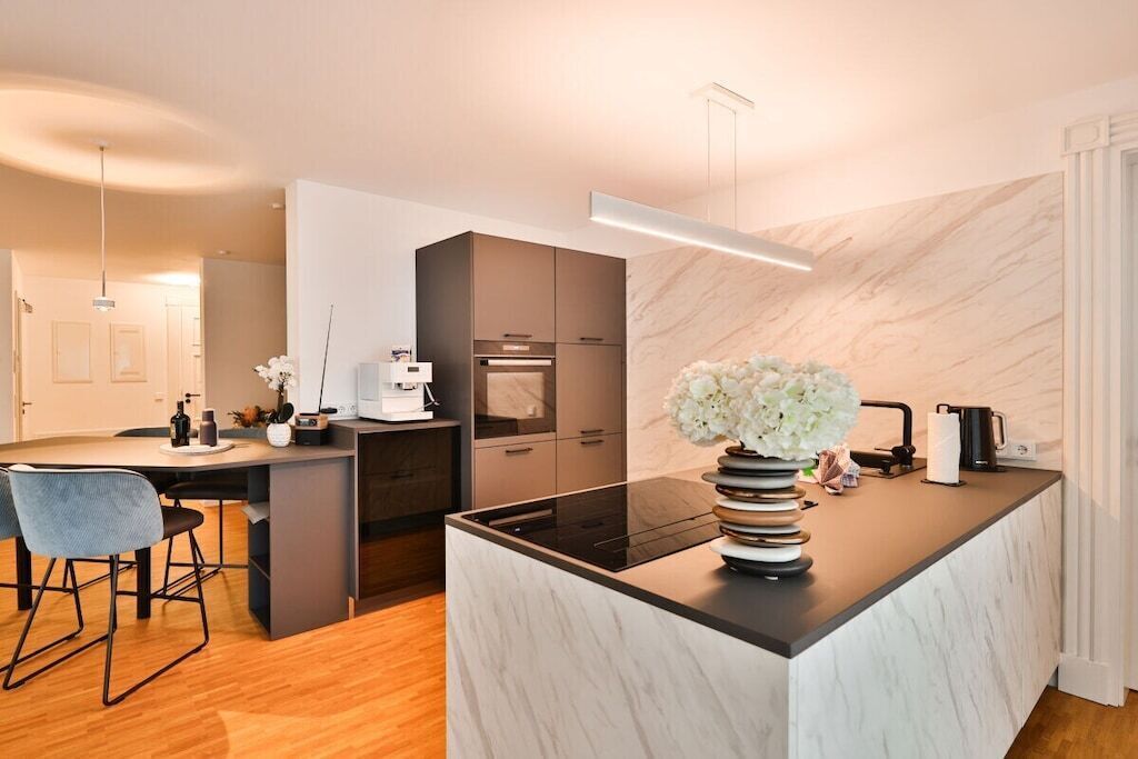 A modern kitchen with a central island, built-in appliances, and a marble backsplash.