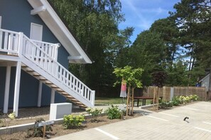 Ein Wohngebäude mit weißer Treppe, einem eingezäunten Garten und einem Parkplatz.