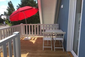 A wooden deck with a white railing, a red umbrella, and a white table with chairs. - Holiday apartment with 2 bedrooms (Röbel\/Müritz)