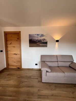 Una habitación con puerta de madera, un cuadro en la pared, un sofá y una lámpara de pie.