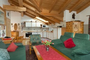 A cozy living room with a green sofa, a wooden dining table, and a kitchen in the background. - Christine Penners 2 - "Kampenwand" (Aschau i. Chiemgau)
