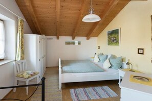 Ein Schlafzimmer mit einem Bett, einem Sessel, einem Schreibtisch und einem Fenster mit Vorhängen.