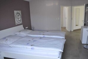 A hotel room with two beds, a white desk, and a door leading to another room. - Holiday apartment with 2 bedrooms (Landkern)