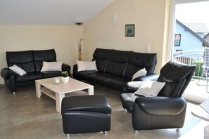 Een woonkamer met twee zwarte leren banken, een witte salontafel en een zwarte leren poef.