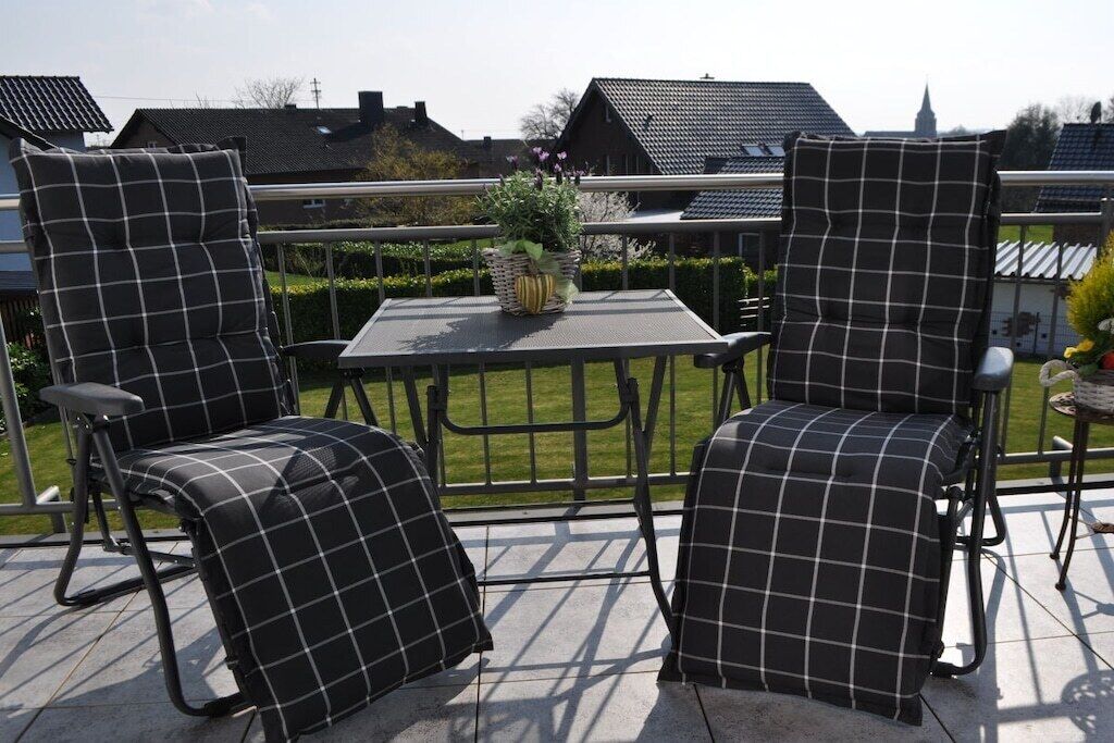 Un espace extérieur aménagé avec deux chaises et une table, entouré d’une rambarde en métal.