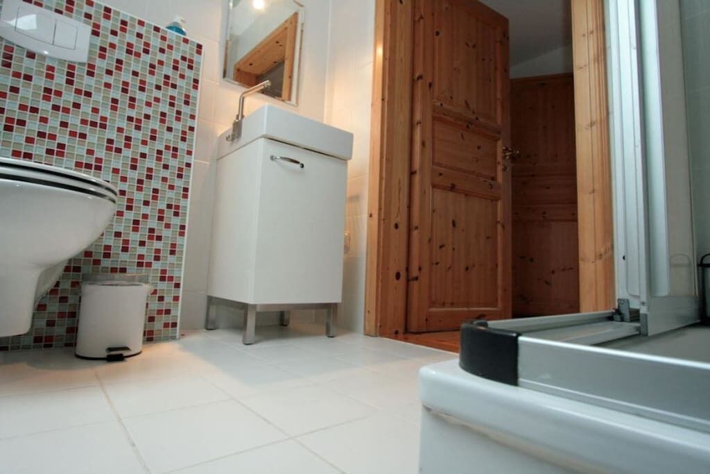 A bathroom with a white sink, a mirror, a toilet, and a wooden door.