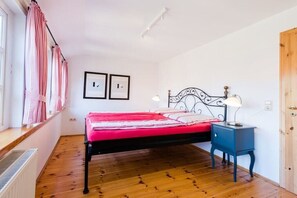 Un dormitorio con cama, una mesita de noche, una ventana con cortinas y dos cuadros en la pared.