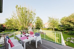 A deck with a table and chairs, surrounded by a white railing, overlooking a well-maintained garden and a residential area. - Holiday apartment with 2 bedrooms (Krummhörn - Greetsiel)
