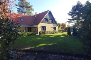 Een herenhuis met een rode pannendak, een verzorgd gazon en een haag op de voorgrond.