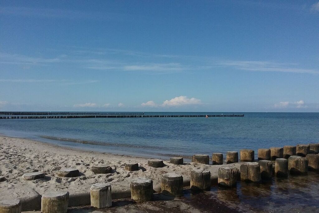 Una playa con un rompeolas de madera y un muelle que se adentra en el agua.