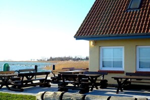 Een gebouw met een pannendak, een raam met zonwering, en een picknickplaats met banken.