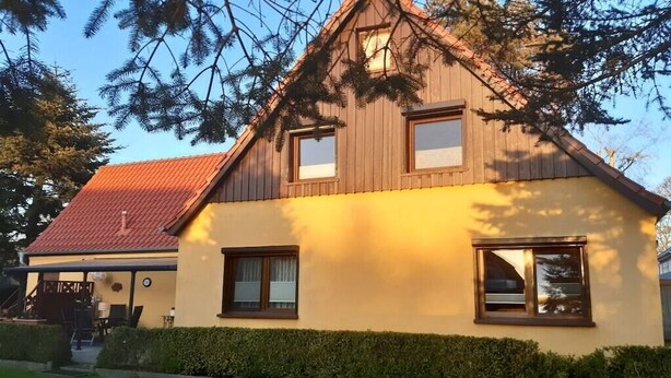 Punaisella katolla, puusivutuksella ja keltaisella julkisivulla varustettu kaksikerroksinen talo.