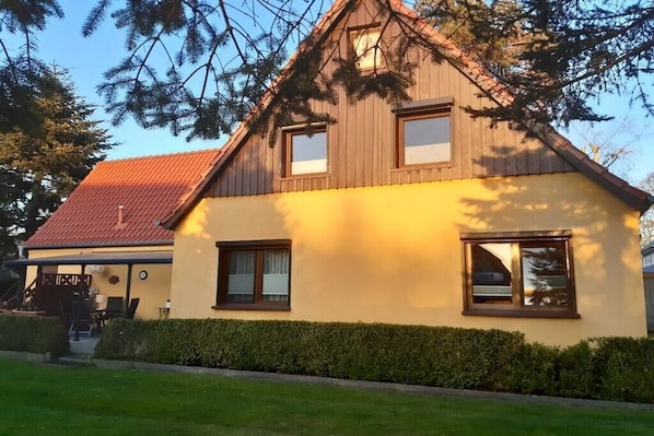 Een huis met twee verdiepingen, voorzien van een rood dak, houten bekleding en een gele gevel.