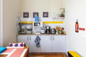 Cocina compacta con microondas, tostadora, cafetera y diferentes utensilios de cocina sobre la encimera.