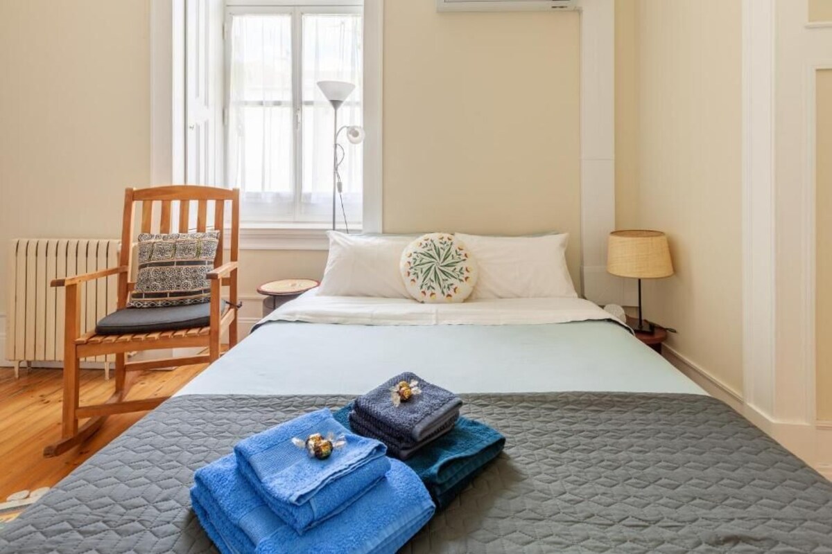 A neatly arranged bedroom with a bed, a chair, a bedside lamp, and a window.