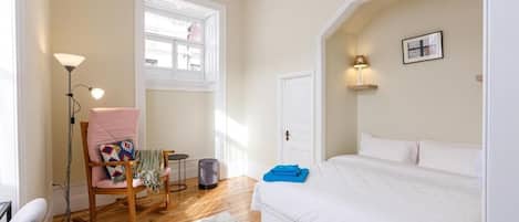 A bedroom with a bed, a chair, a floor lamp, a window, and a door.