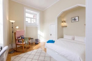 Un dormitorio con cama, una silla, una lámpara de pie, una ventana y una puerta.