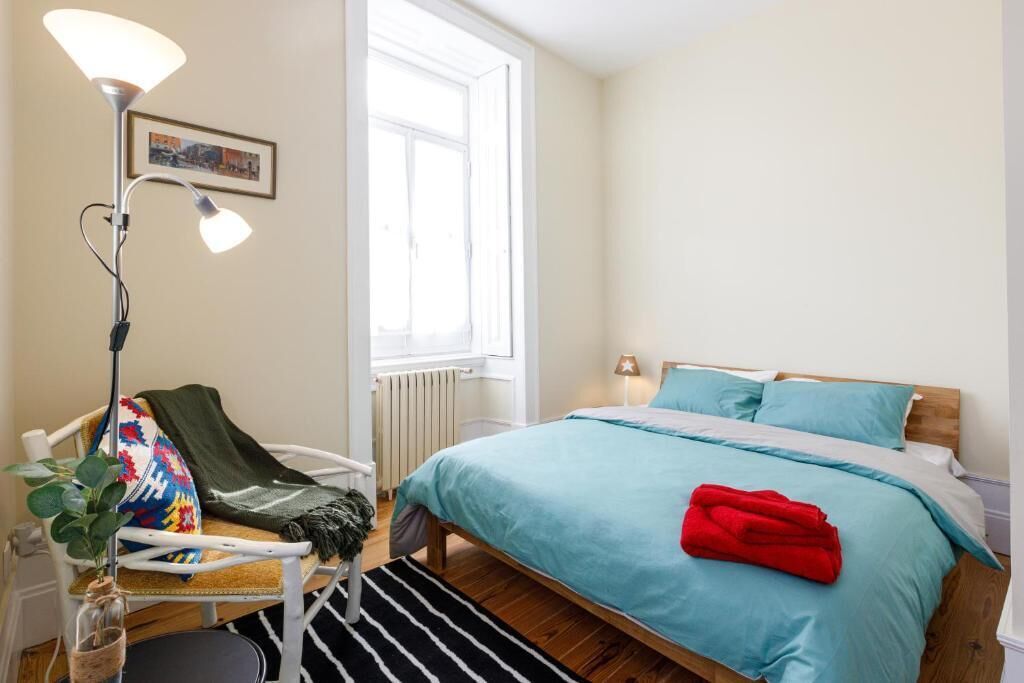 A bedroom with a bed, a chair, a floor lamp, a window, and a radiator.