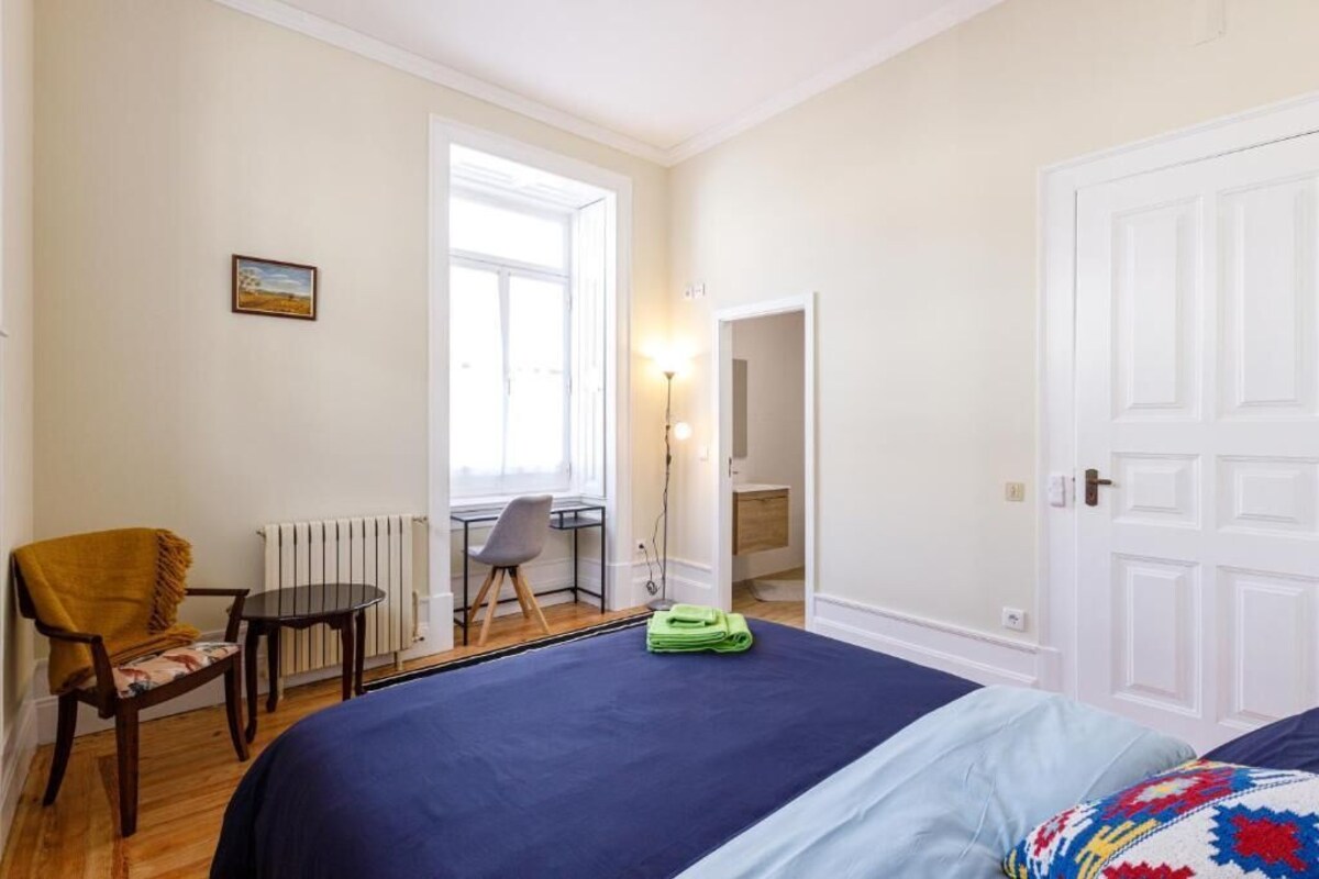 A bedroom with a bed, a chair, a desk, and a radiator.