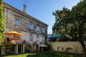 Un patio con un edificio de tejado de azulejos, una hamaca, asientos exteriores y un árbol con frutos.