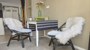 Due sedie con soffici cuscini bianchi, un tavolo a motivi bianchi e neri e un vaso verde con fiori su una parete beige.