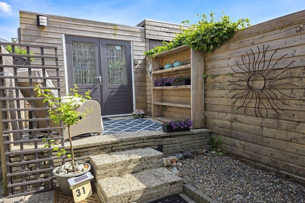 Una valla de madera con un diseño de sol, un pequeño jardín con escalones y una puerta con ventana.