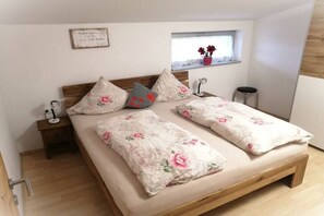 Ein Schlafzimmer mit einem Bett, Kissen, einem Nachttisch, einem Fenster und einem kleinen Hocker.