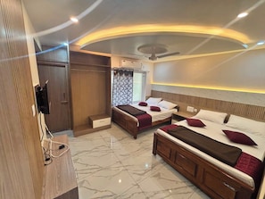 Habitación de hotel con dos camas, televisión, armario y ventilador de techo.