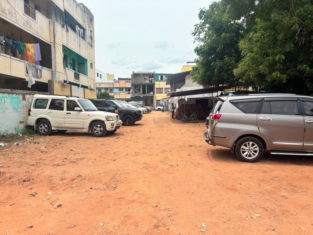 A dirt road with parked cars and buildings in the background.