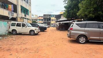 A dirt road with parked cars and buildings in the background.