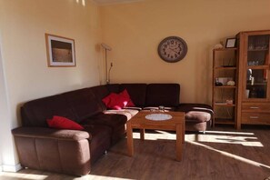 Ein Wohnzimmer mit braunem Sofa, einem Holztisch, einer Wanduhr und einem Bücherregal.