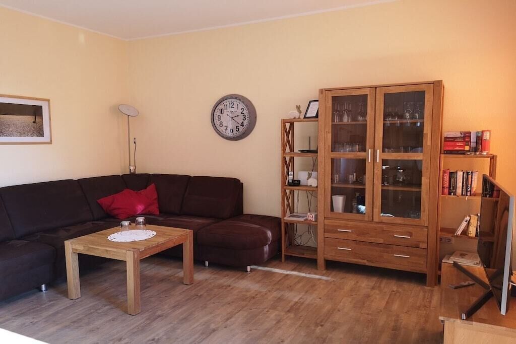 Una sala de estar con un sofá marrón oscuro, una mesa de centro de madera, un mueble de madera con puertas de vidrio y un reloj de pared.