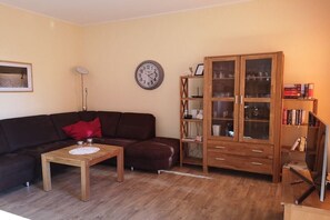 Ein Wohnzimmer mit einem dunkelbraunen Sofa, einem Holztisch, einer Holzkabine mit Glastüren und einer Wanduhr.
