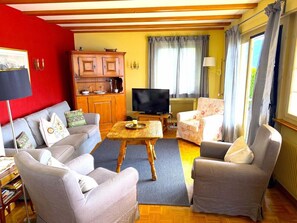 A living room with a sofa set, a coffee table, a television, and a kitchen area with cabinets and a stove.