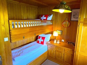 Une chambre avec un lit superposé en bois, une table de chevet, une lampe et un tableau encadré au mur.