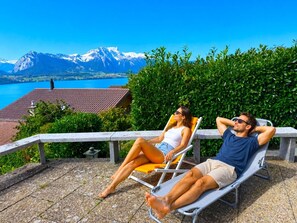 Two people relaxing on lounge chairs with a mountain and lake view. - Concierge, Lake Thun/Alps Scenic Views by SwissHut (Sigriswil)