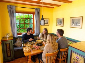 Un coin repas avec une table dressée pour quatre personnes, une fenêtre avec des rideaux et une vue sur la verdure à l’extérieur.