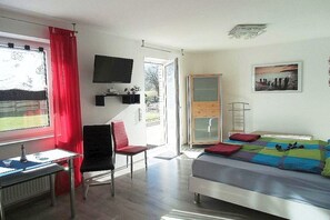 A bedroom with a bed, a desk, a chair, a TV, and a window with curtains. - Holiday apartment with 1 bedroom (Wiesmoor)