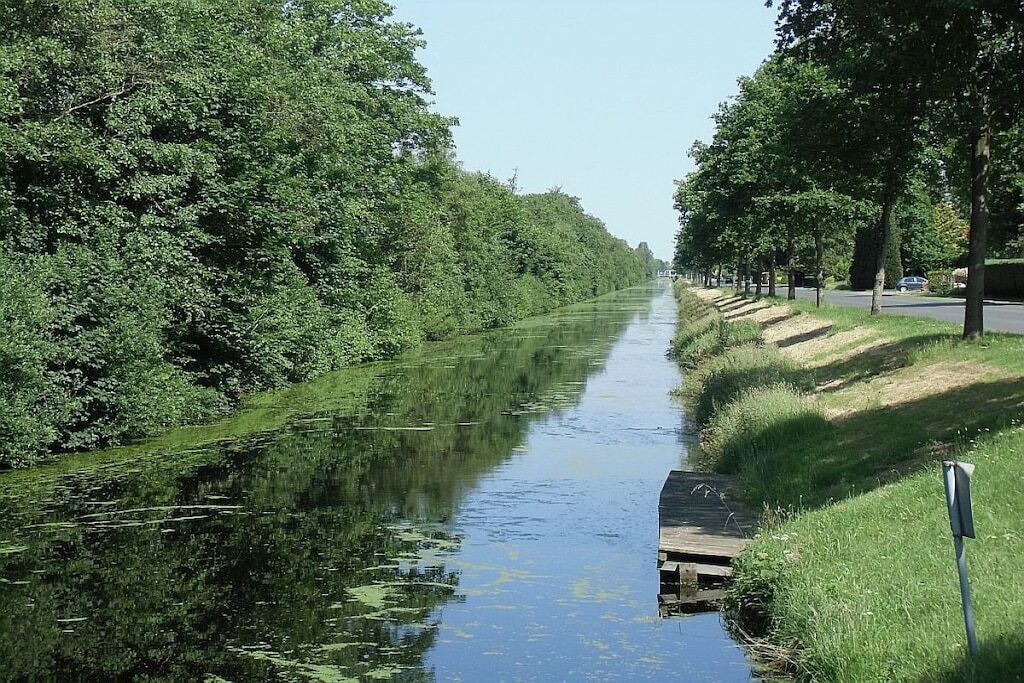 Un canal estrecho bordeado por densa vegetación y un camino pavimentado.