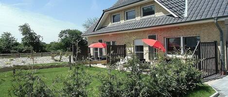 A two-story house with a sloped roof, a fenced backyard, and two red umbrellas.