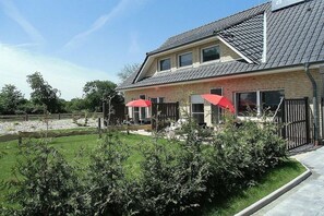 A two-story house with a sloped roof, a fenced backyard, and two red umbrellas. - Holiday apartment with 1 bedroom (Wiesmoor)